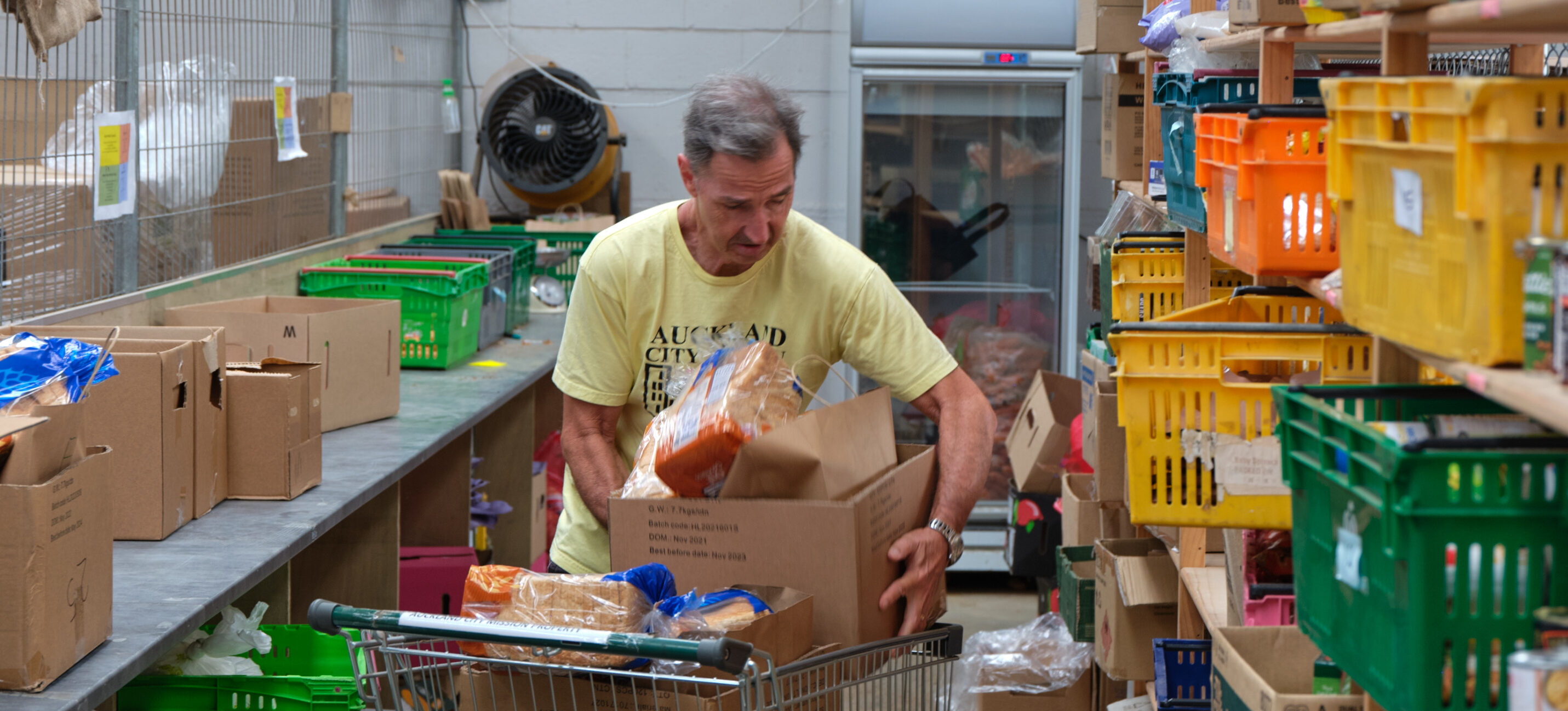 Volunteer Mike packing food parcels into a trolley for collection at Auckland City Mission Food Security.